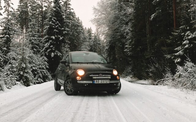 Auto auf einer schneebedeckten Straße zwischen Nadelbäumen im Winter