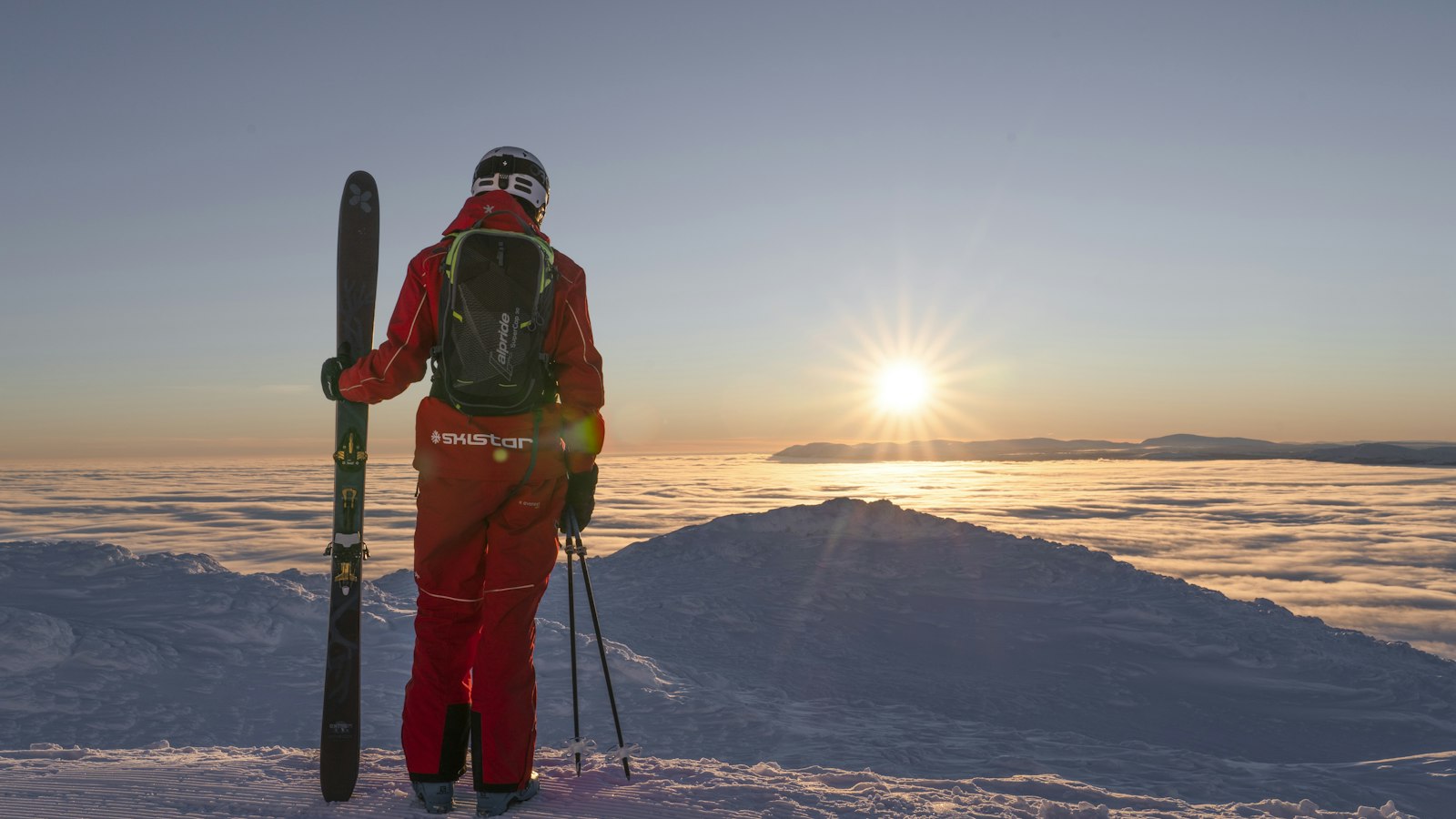 A skier holding skis at sunrise above a cloud inversion in Åre